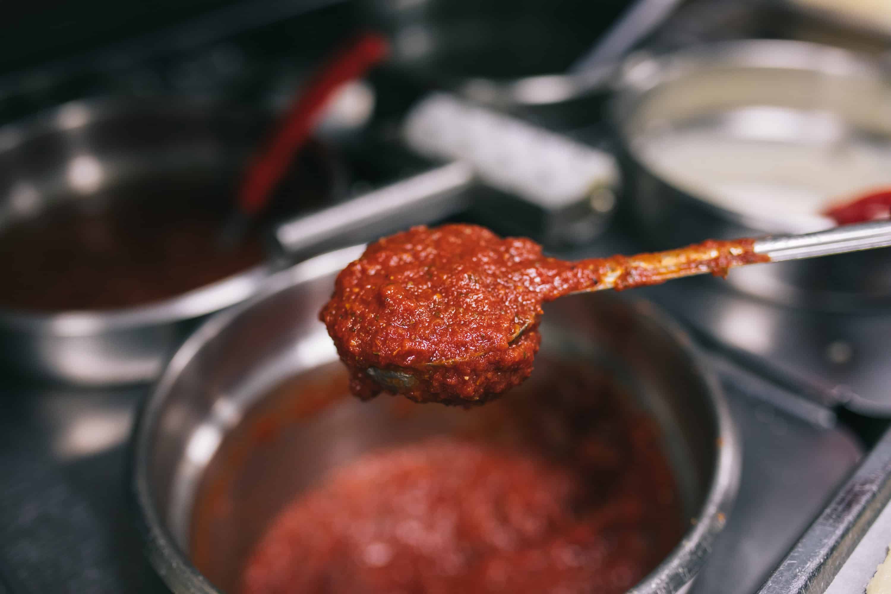 pizza sauce in a ladle over a silver pot